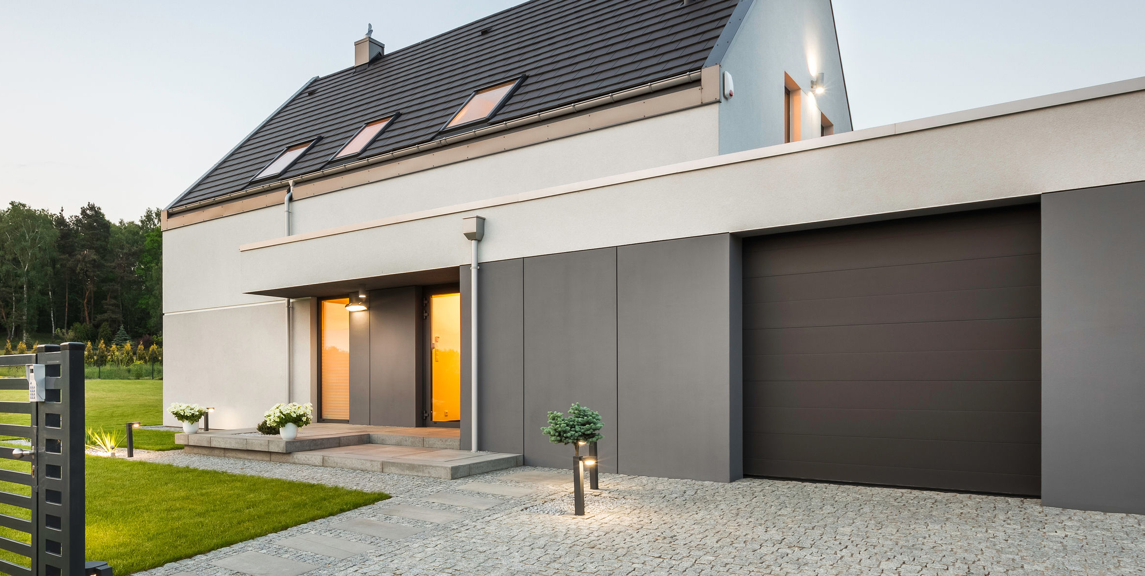 External view of stylish family house with fence, garage, stone driveway and garden, panorama